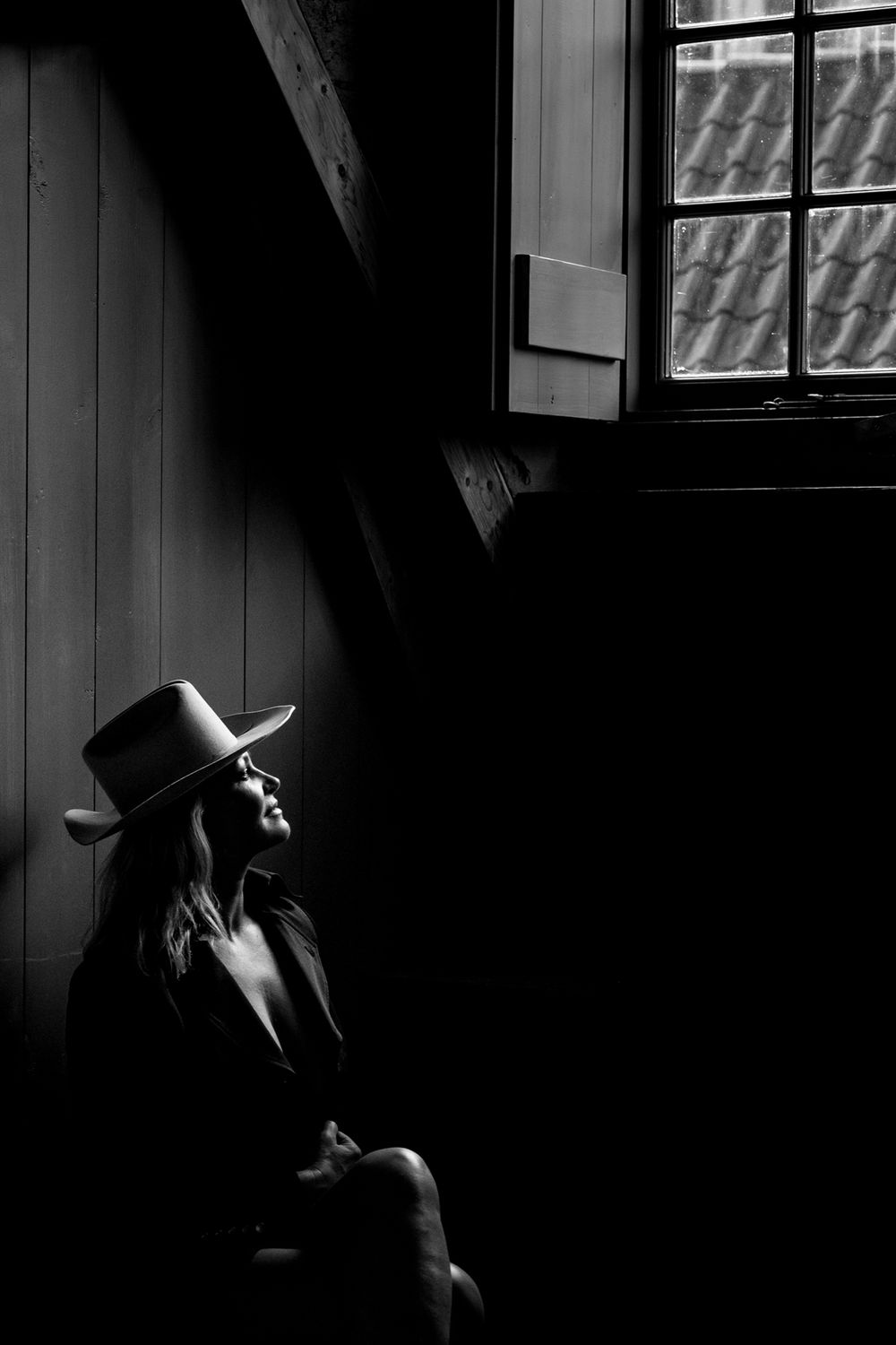 A dramatic black and white profile silhouette of a cowboy hat wearing figure by a window in dark moody lighting.