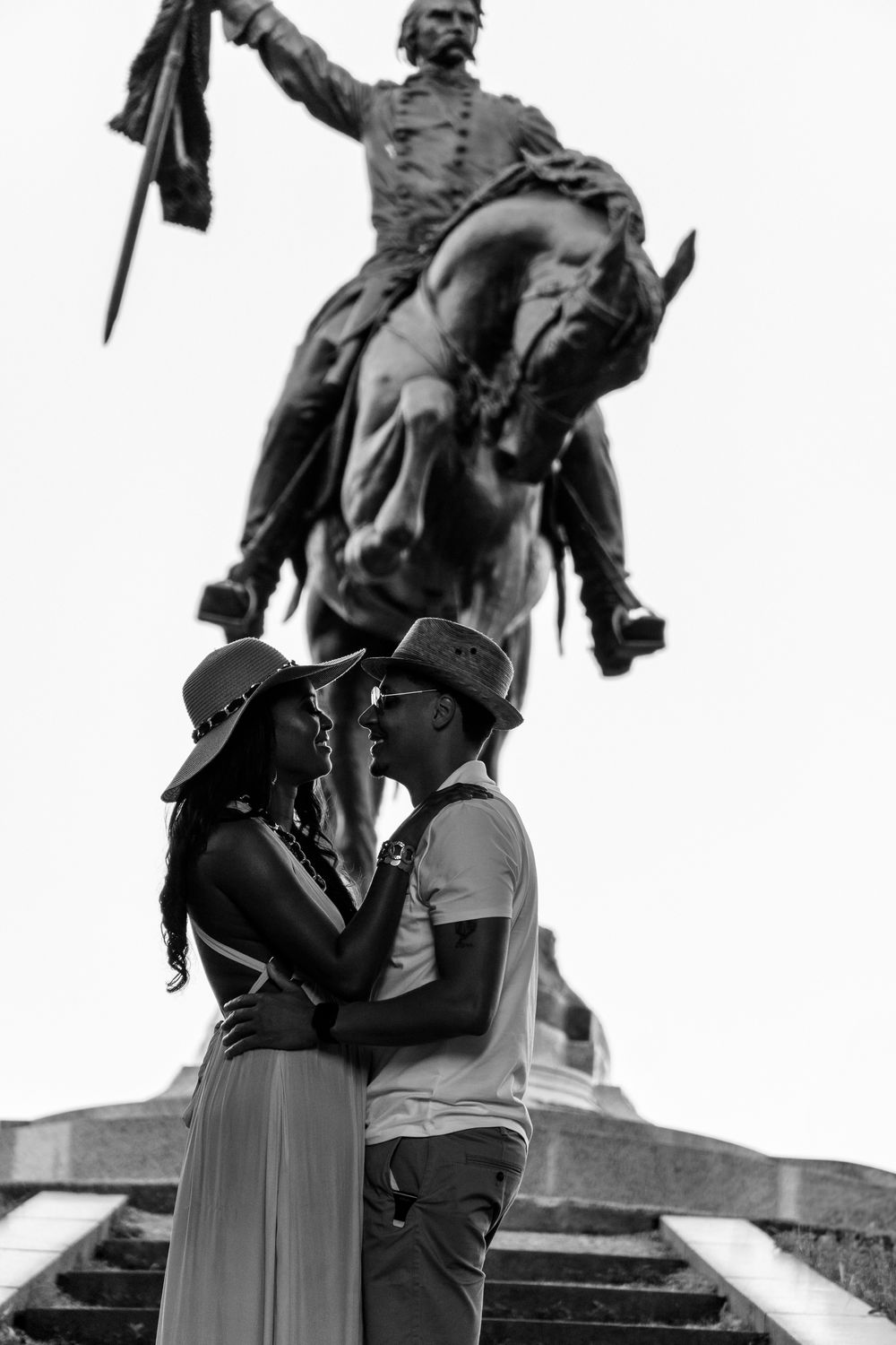 Couple embracing in front of equestrian statue in black and white.