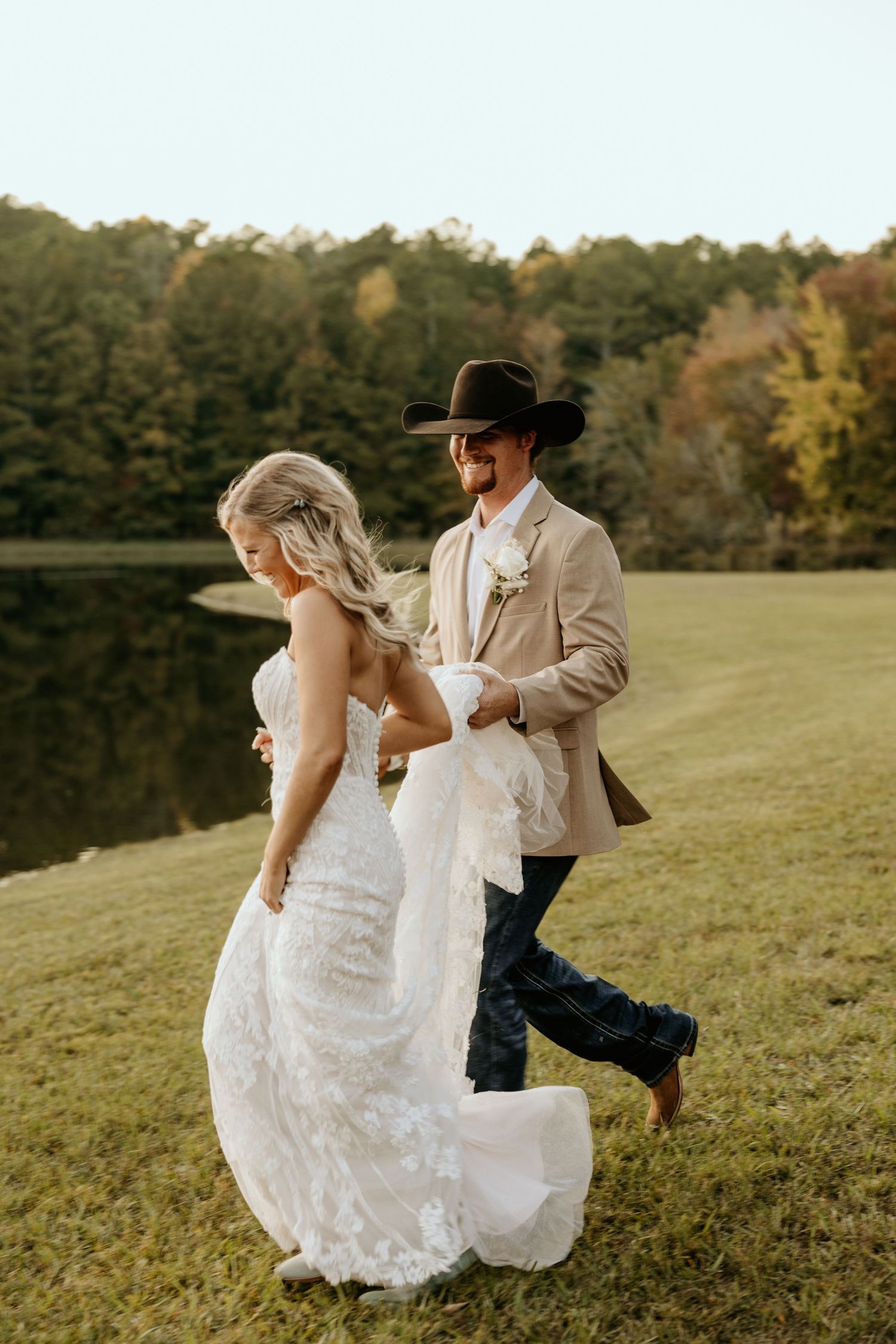 Couple in wedding attire playfully walking by a lake during golden hour photography session.