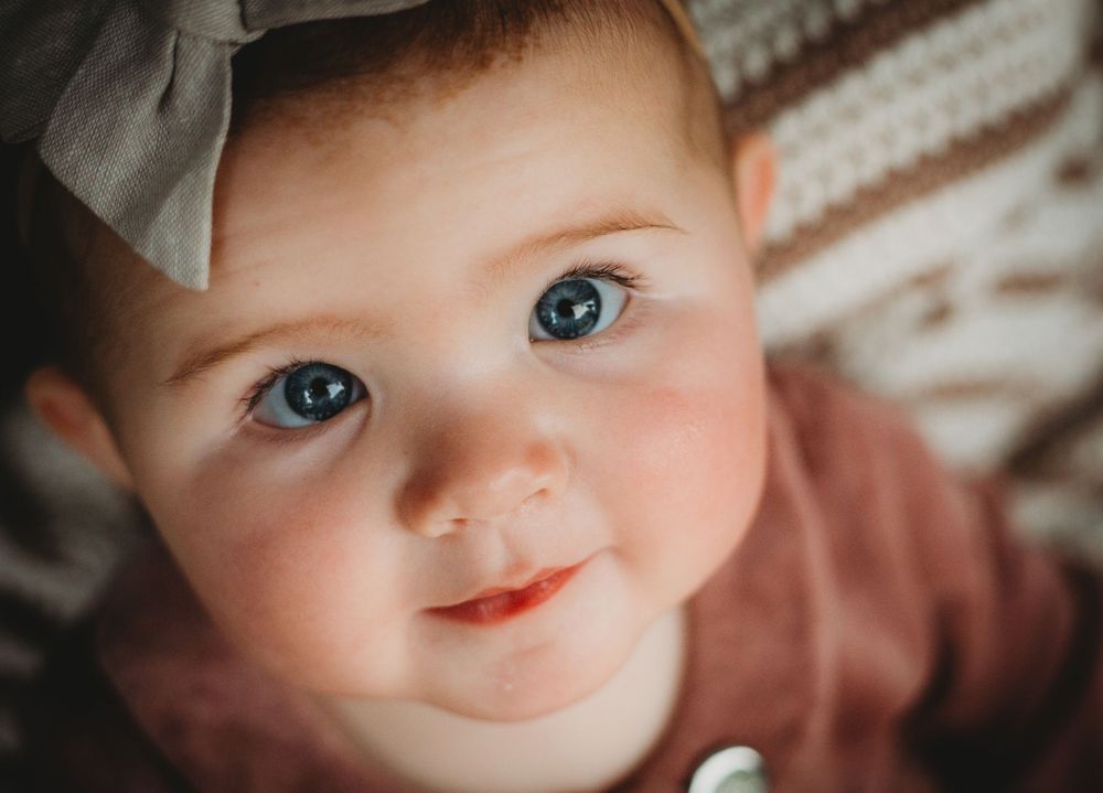 Close-up portrait showing bright blue eyes and rosy cheeks with soft lighting.