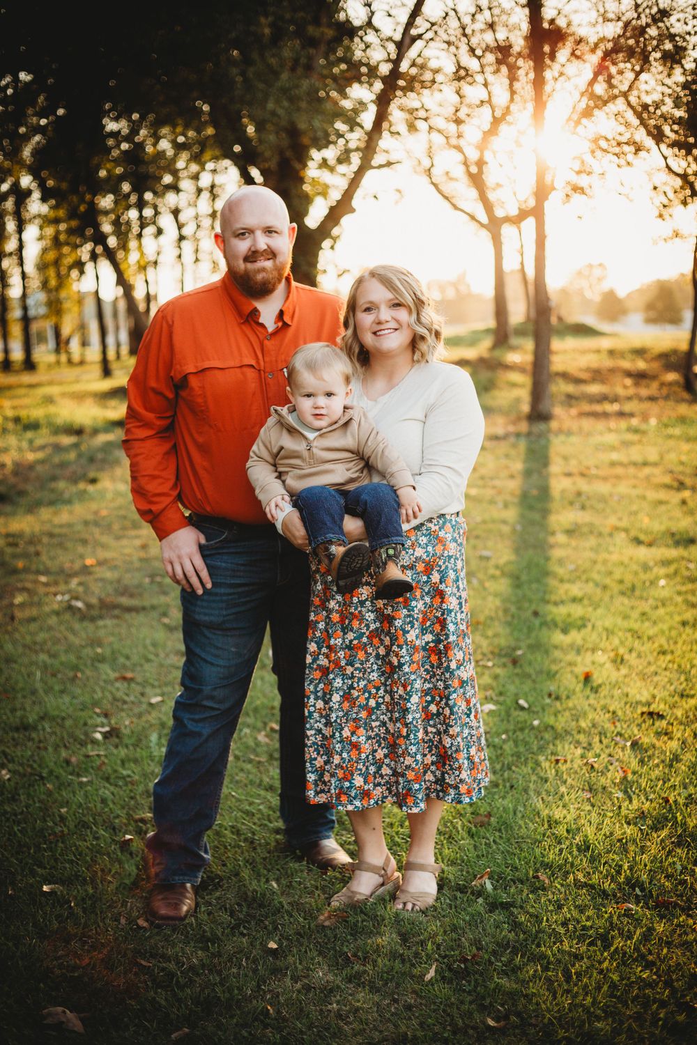 Family portrait at sunset in a park with golden sunlight filtering through trees.