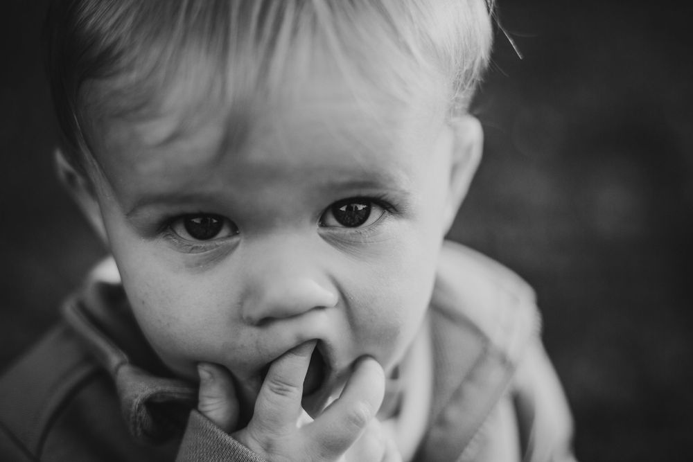 Black and white close-up portrait of young child with fingers near mouth.