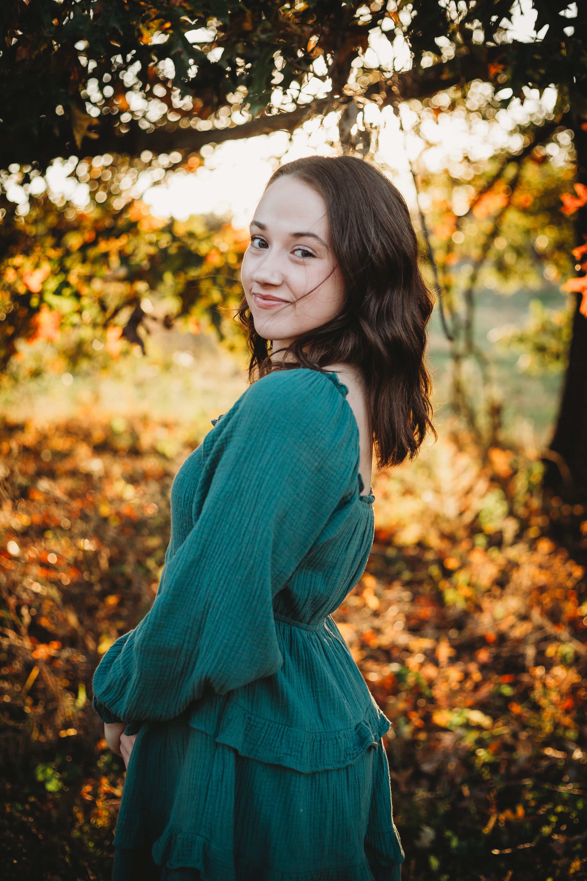 A portrait in a teal dress against autumn foliage during golden hour.