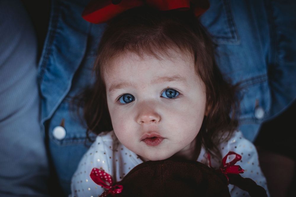 Close-up portrait of toddler with bright blue eyes wearing red bow.