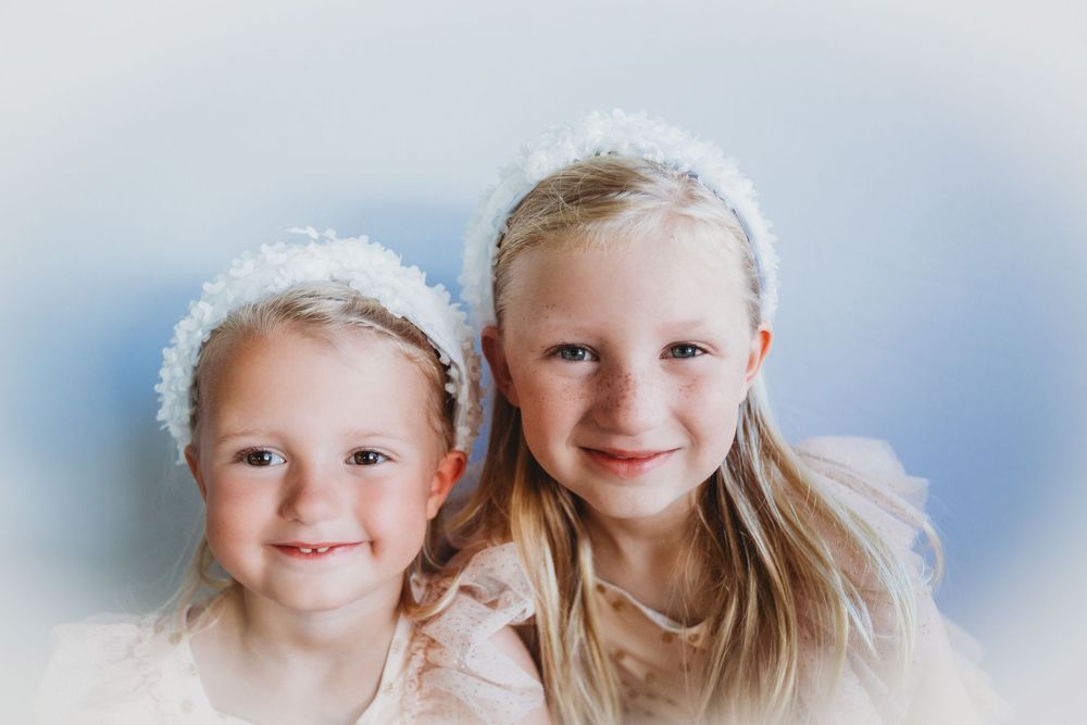 Five children wearing white clothing smile together in a bright studio setting against a blue background.