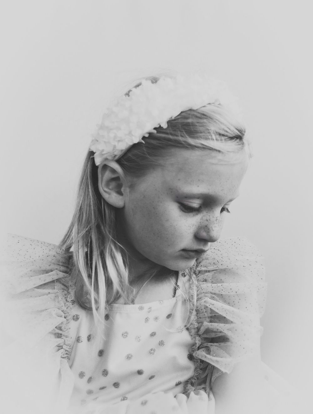 Black and white portrait showing a downward gaze and delicate lace details in a soft, ethereal style.