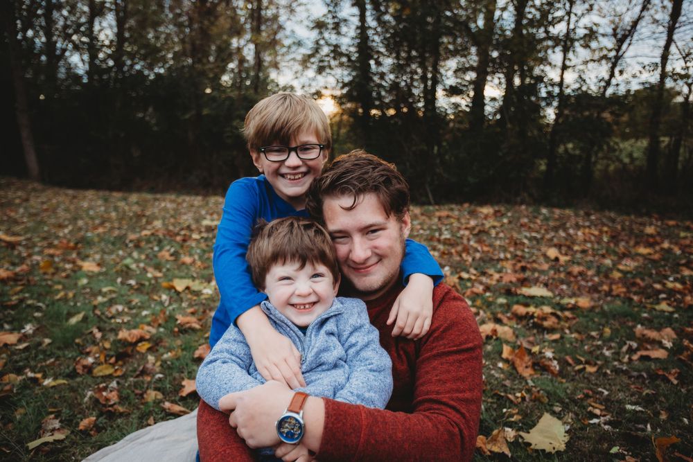 A heartwarming family portrait session in a fall forest with colorful autumn leaves scattered on the ground.