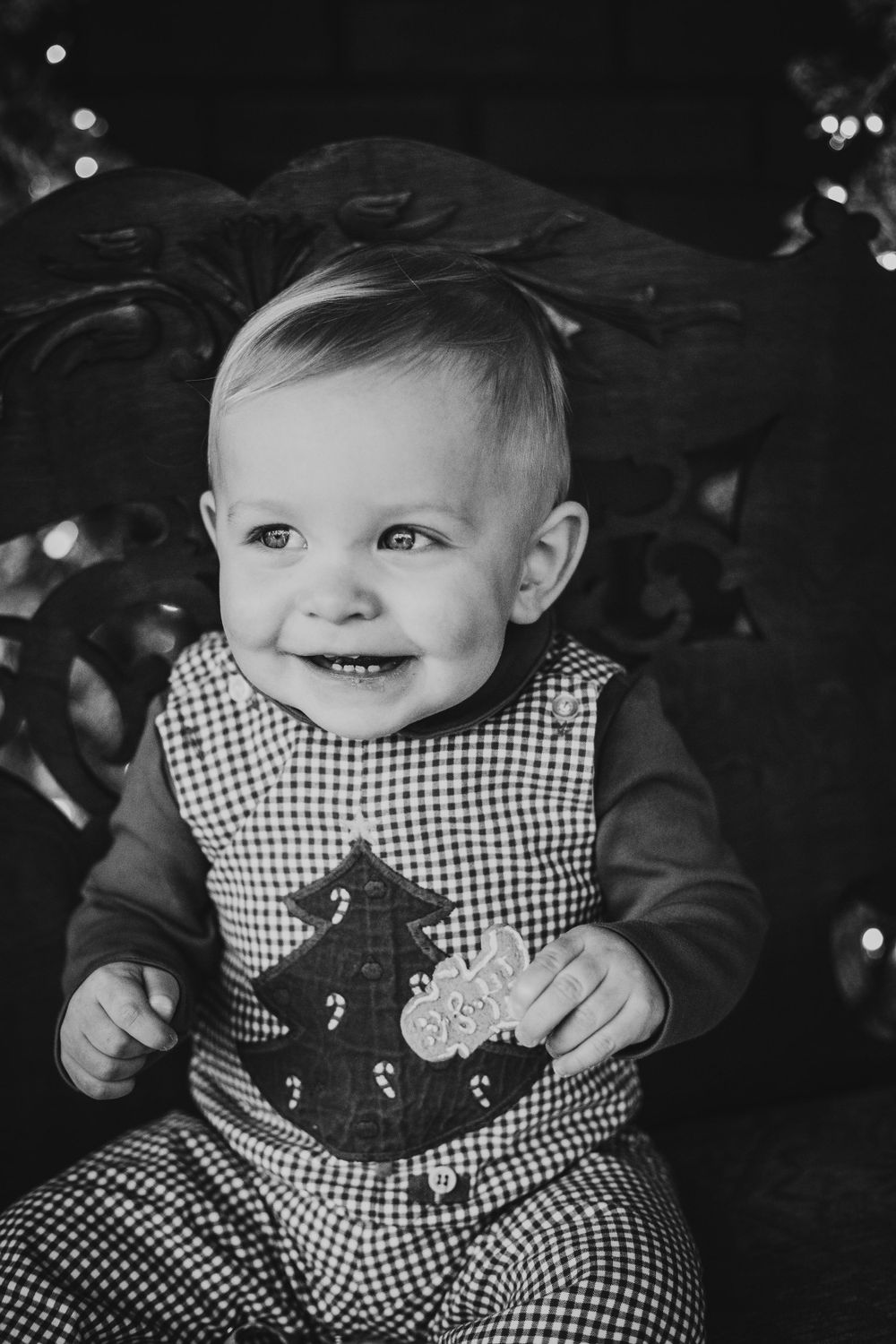 Smiling baby in checkered overalls with holiday decorations in background.