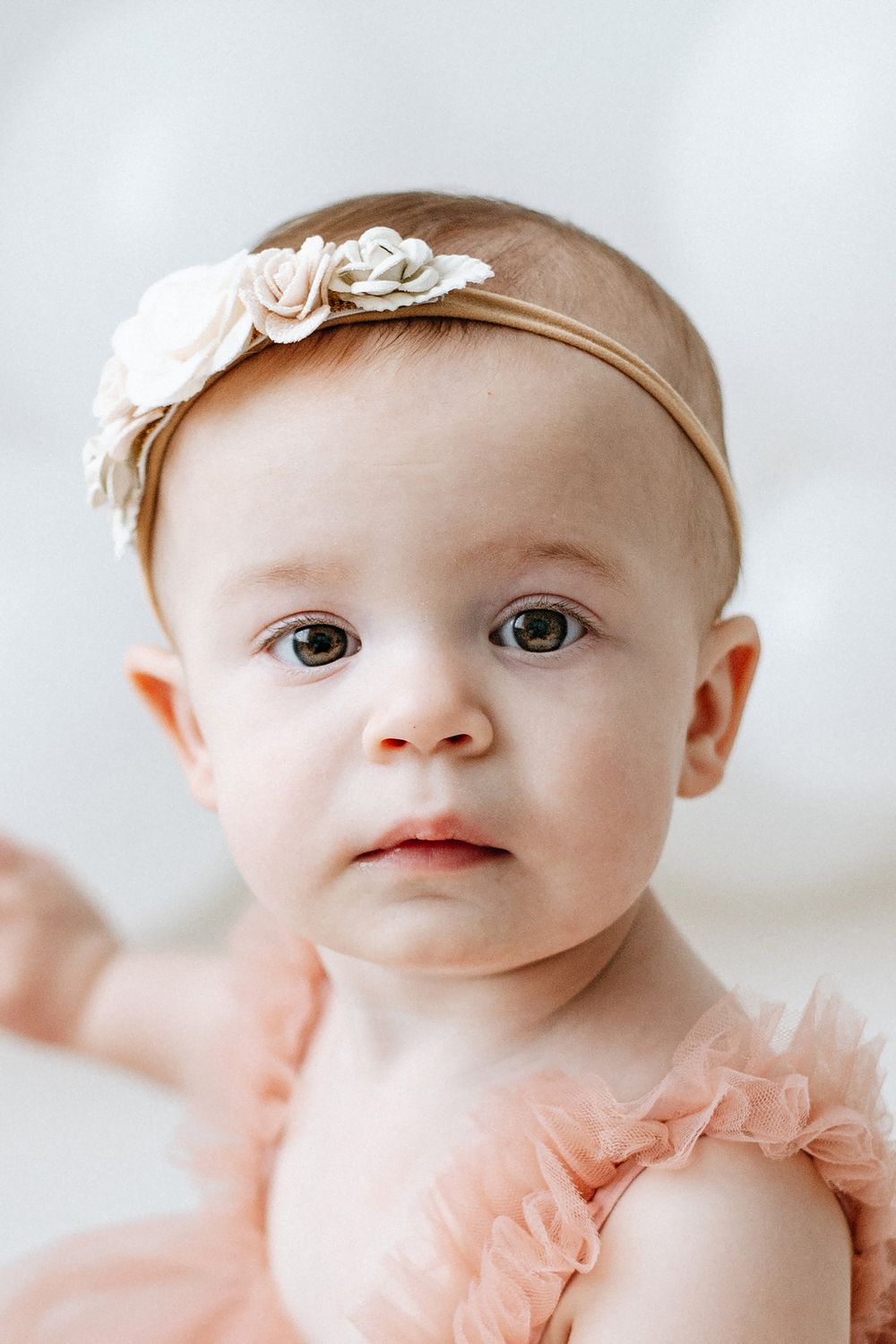 Sweet baby wearing a pale pink tulle dress and delicate floral headband in soft portrait photography.