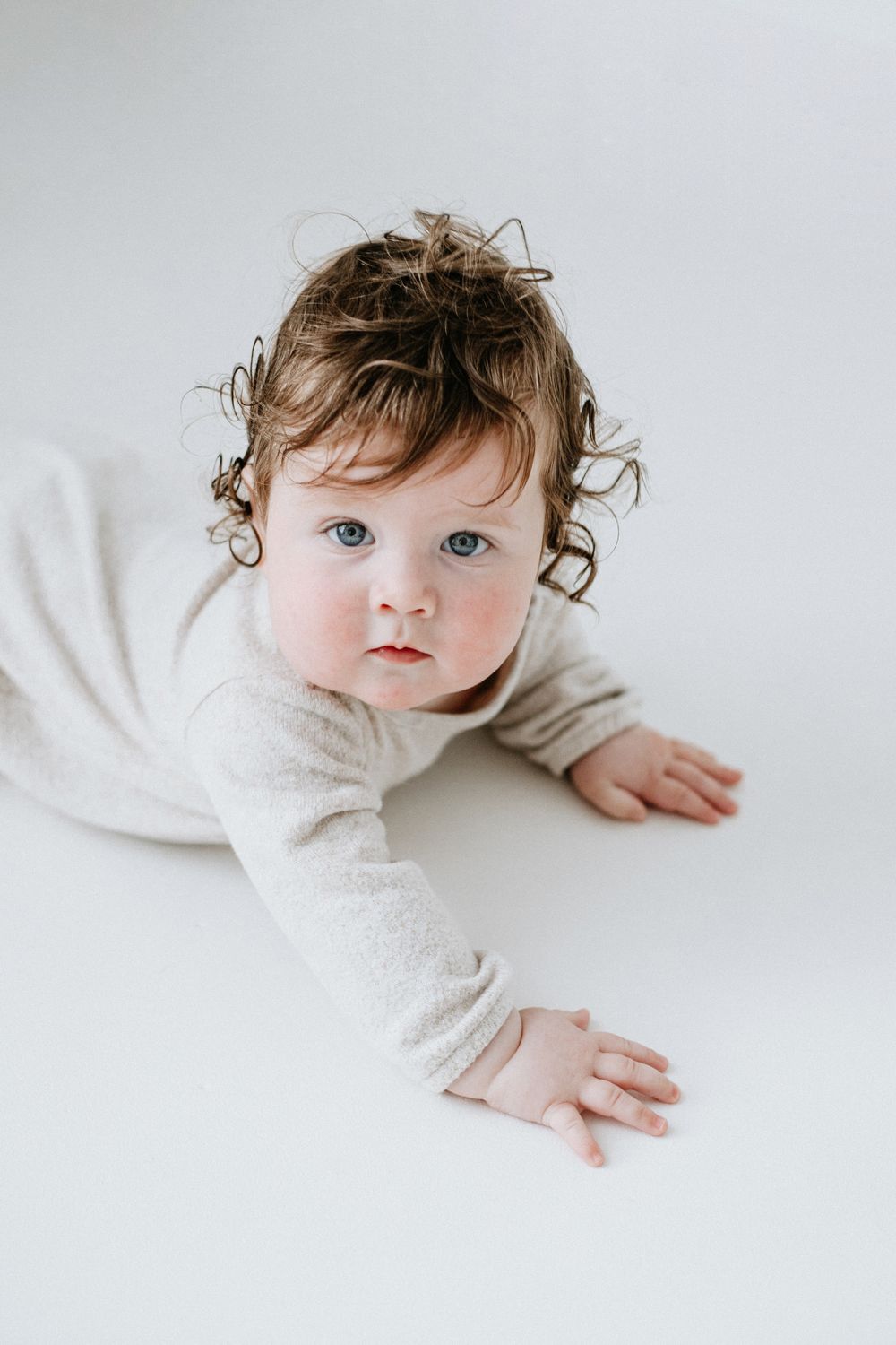 Baby in white sweater lying on white background with curly brown hair.