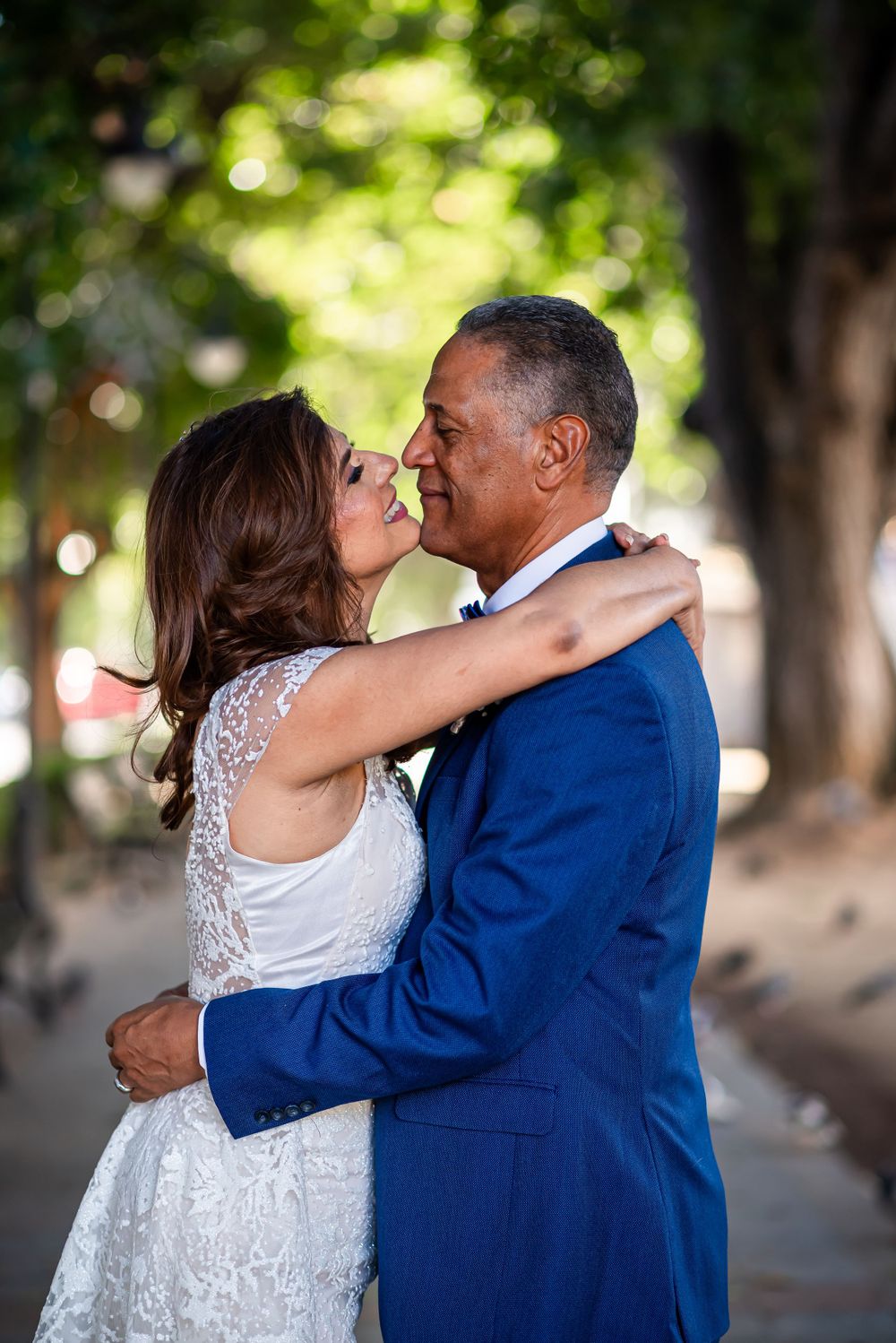 Couple shares passionate kiss during wedding photoshoot in a sunlit park setting.