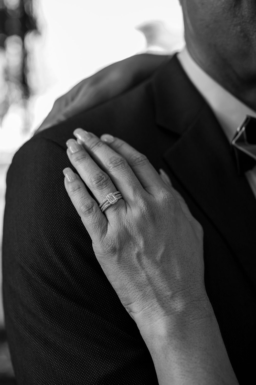 Close-up black and white shot of bride's hand with wedding ring resting on groom's shoulder.