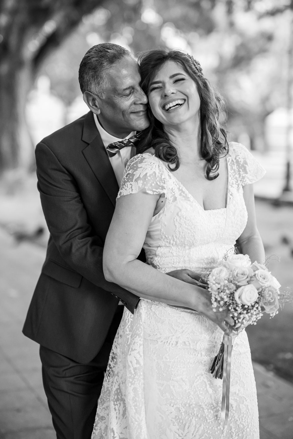 Black and white portrait of joyful couple sharing intimate moment with bride holding bouquet.