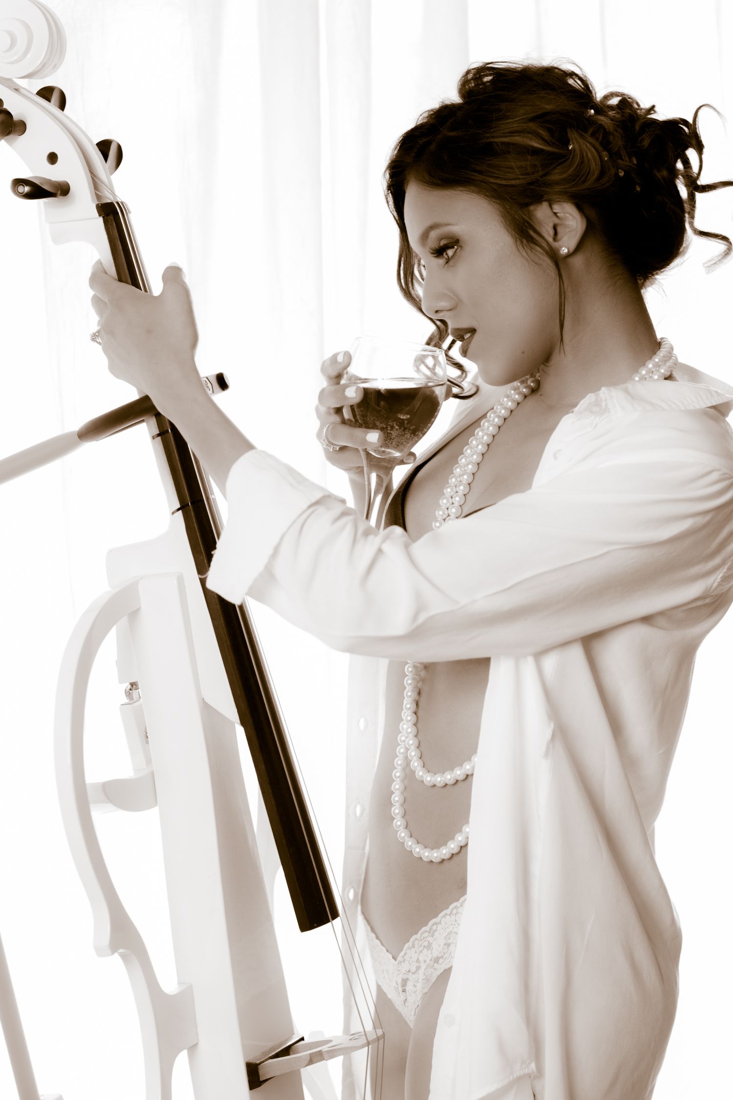 Sepia toned portrait with cello, pearls and white robe in artistic composition.