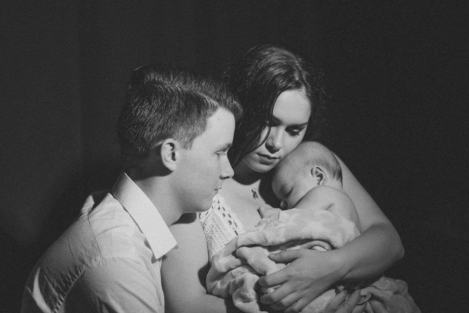 Intimate black and white photograph showing family sitting close together with their young baby.