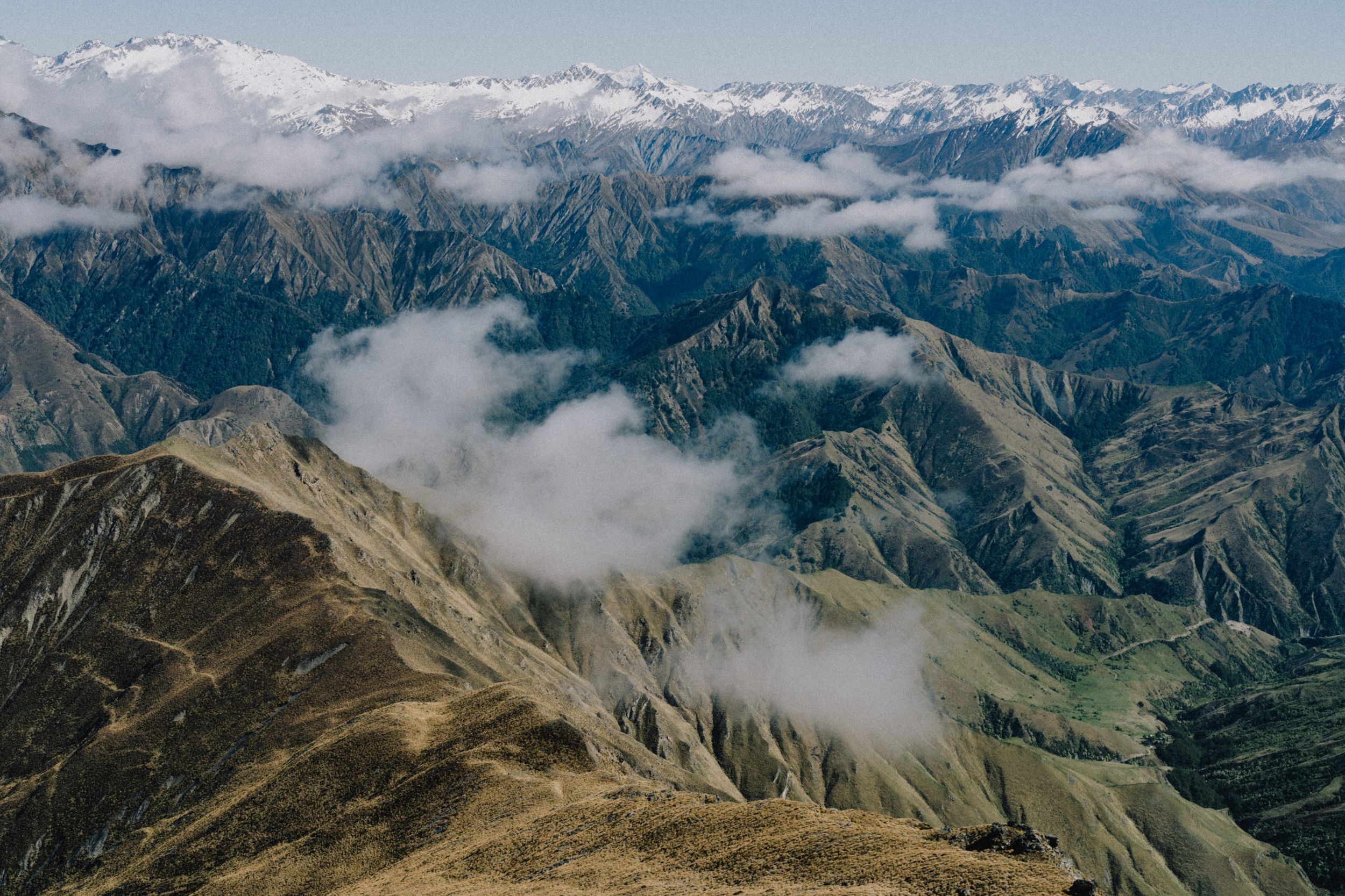 Aerial view of rugged mountain ranges with clouds drifting through valleys below.