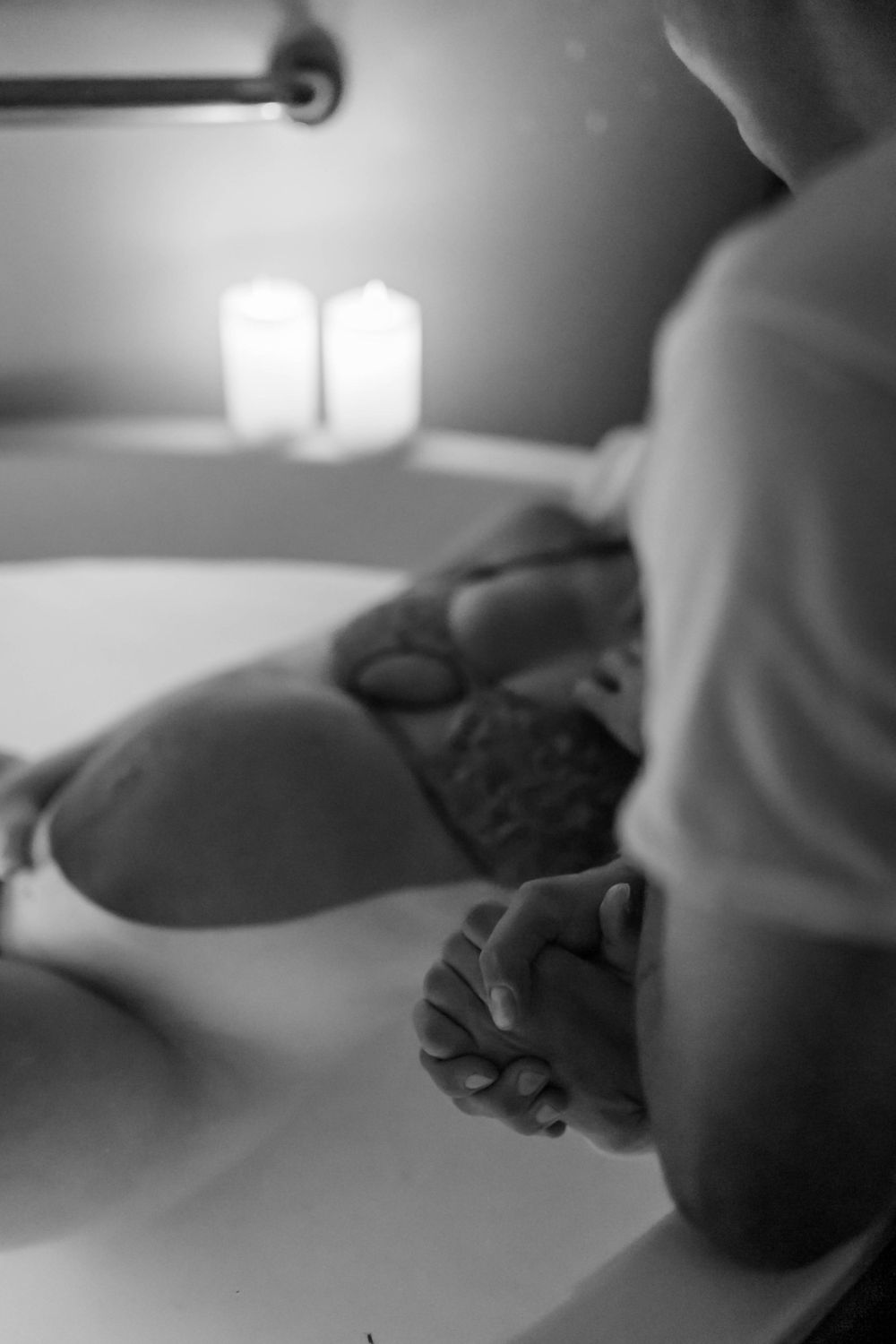 Close-up black and white photo of a pregnant belly with hands resting gently on top.