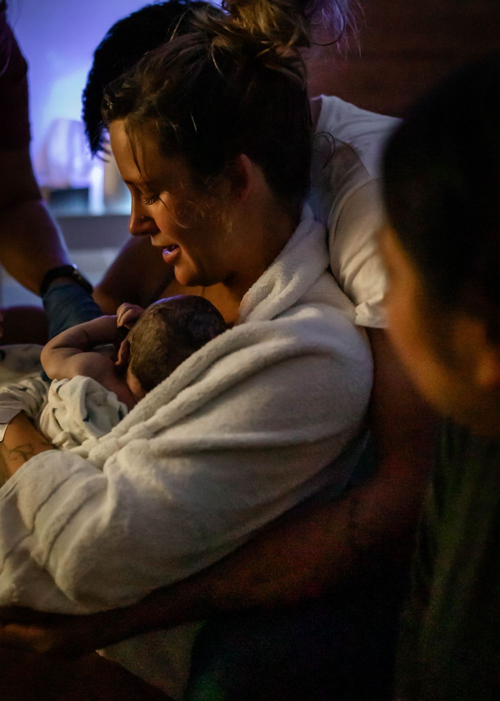 Tender moment of a newborn being held in soft lighting.
