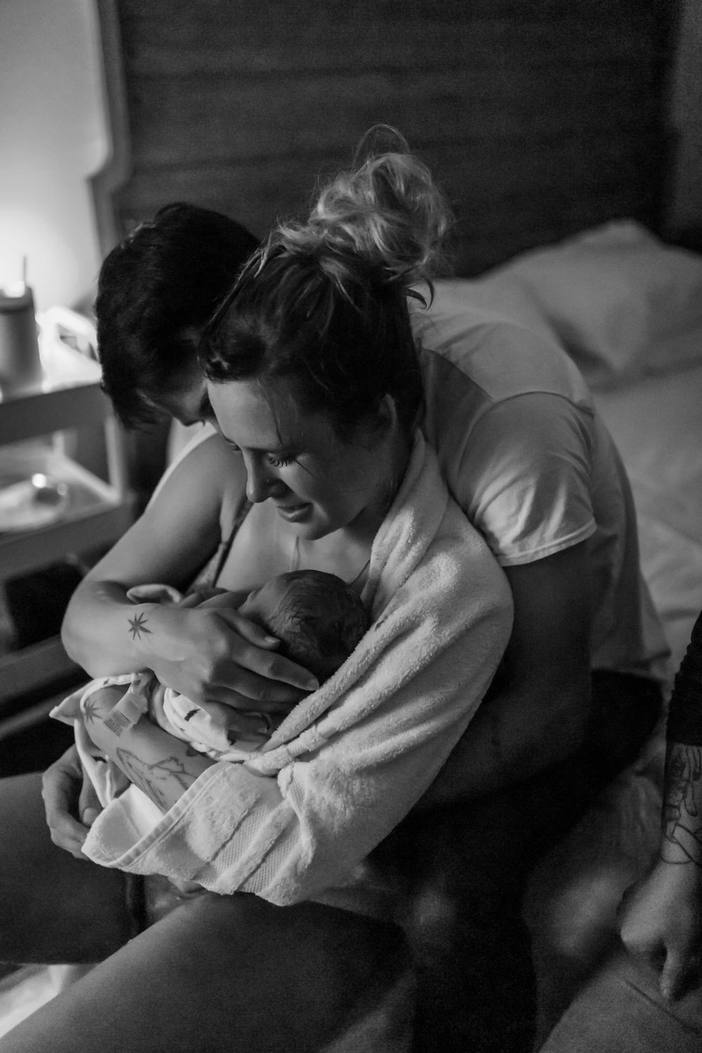 Intimate black and white portrait of a newborn being cradled in gentle embrace.