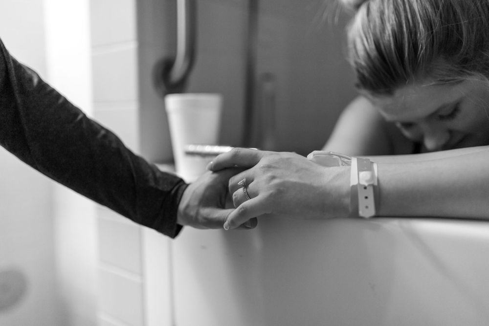 Black and white image showing hands clasped together in support during labor.