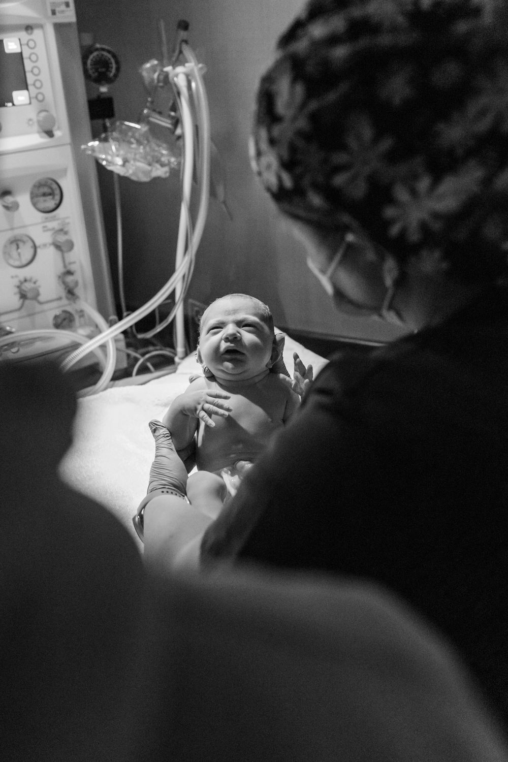 A newborn baby lies in a hospital bassinet while being examined by medical staff.