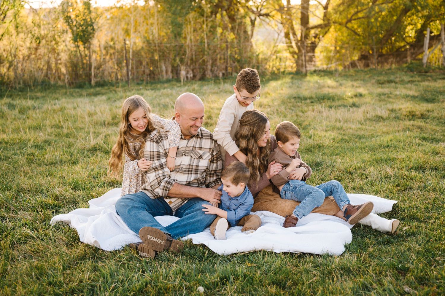 A group sits together on a white blanket in a sun-dappled meadow during golden hour.