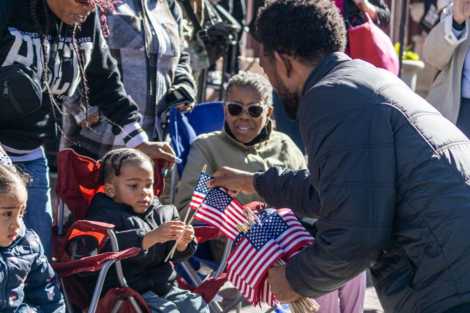 A group gathering and parade outdoors with children holding American flags.