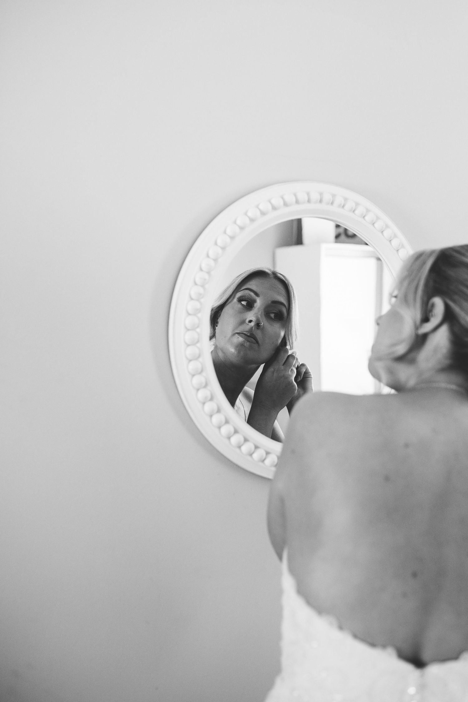 White ornate mirror on wall reflecting person getting ready.