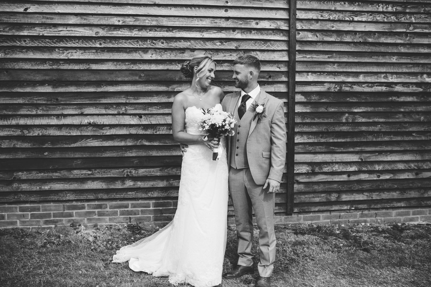 A series of black and white wedding photos showing intimate moments between a couple against a rustic wall backdrop.