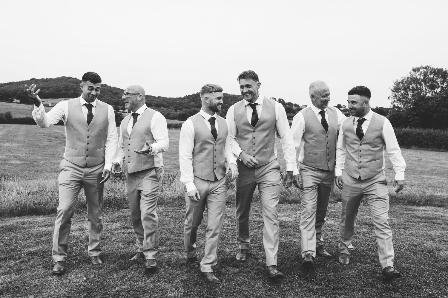 Groomsmen in light colored suits strike playful poses while kneeling on grass.