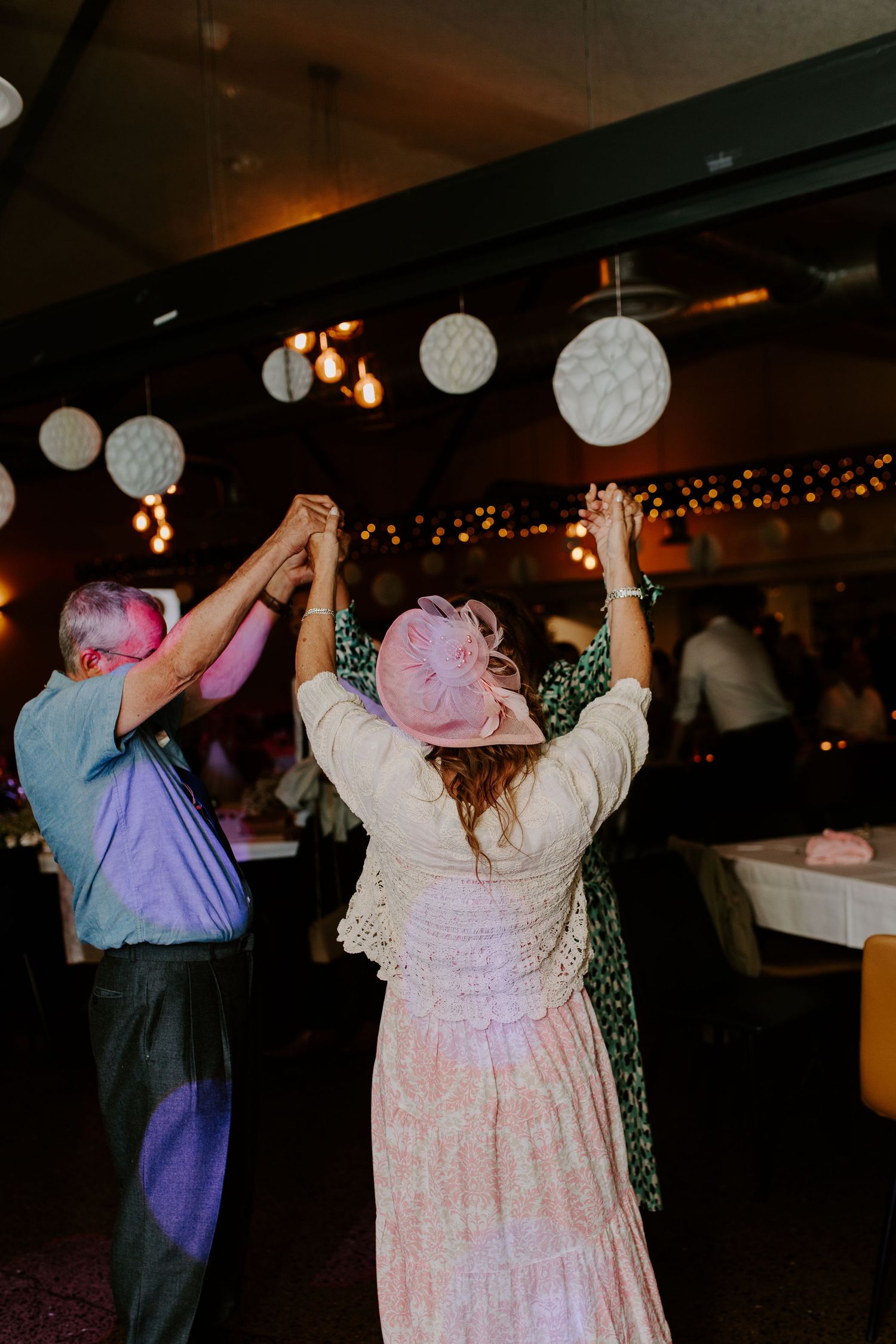 A couple dances together at a reception venue decorated with white paper lanterns and string lights.
