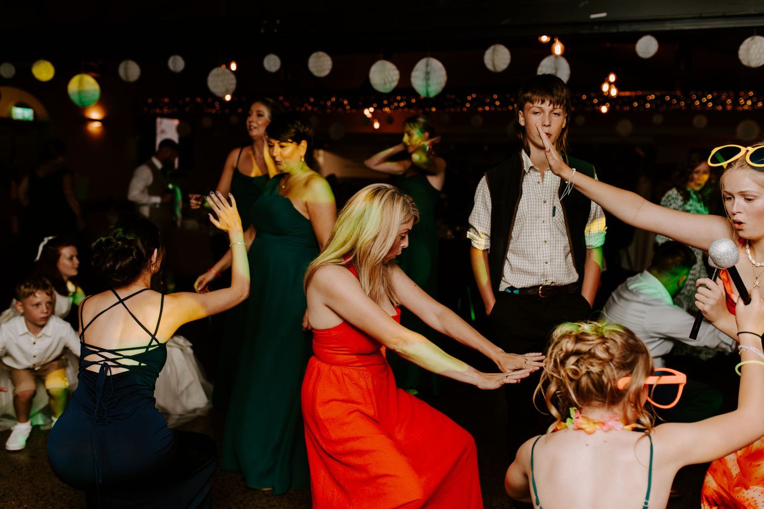 Wedding reception dance floor filled with guests celebrating under dim lighting with colorful balloons.