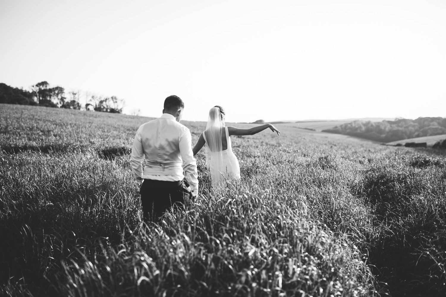 A black and white wedding photo of a couple walking away on a path under string lights. Larmertree