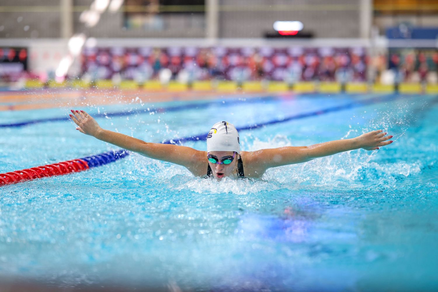 Swimmer performing butterfly stroke during competition with arms spread wide.