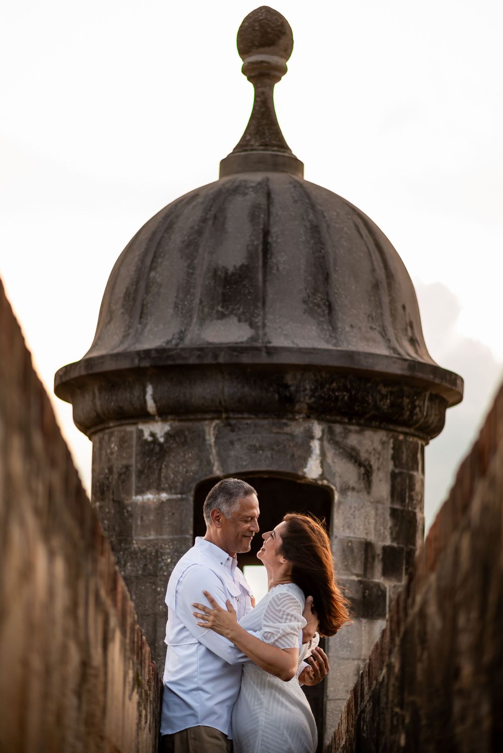 Romantic couple embracing beneath historic stone guard tower at sunset in Old San Juan.