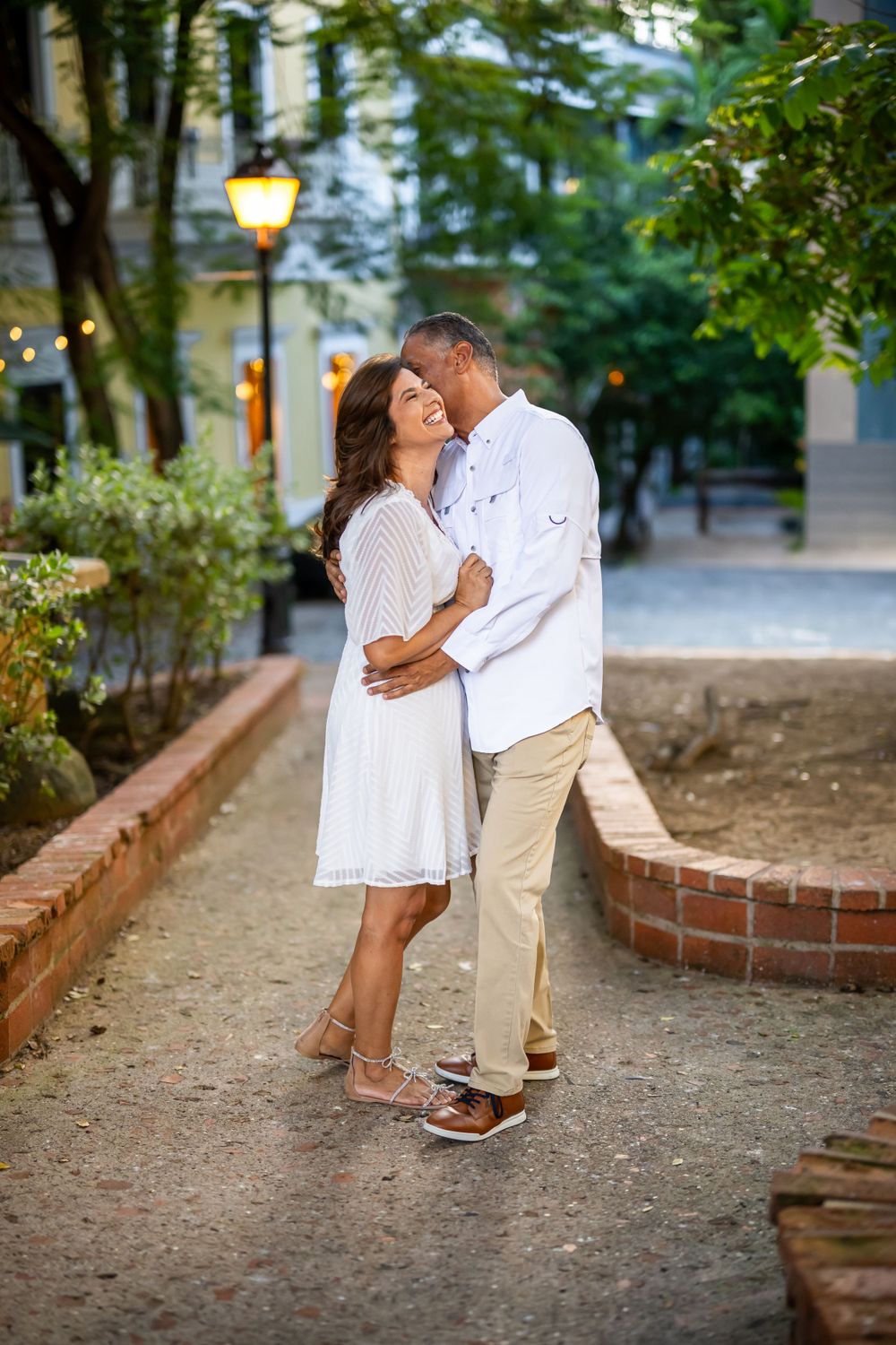 Couple embracing on romantic path with glowing lamp post at dusk.