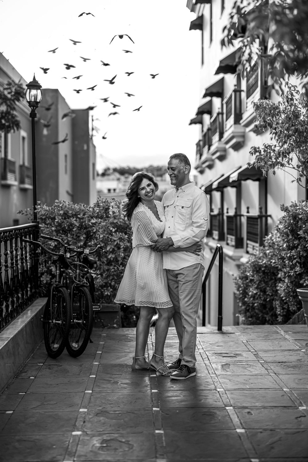 Black and white photo of couple dancing with birds flying overhead in historic district.