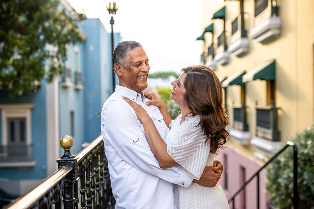 Couple in white clothing embracing on historic balcony with colonial architecture.