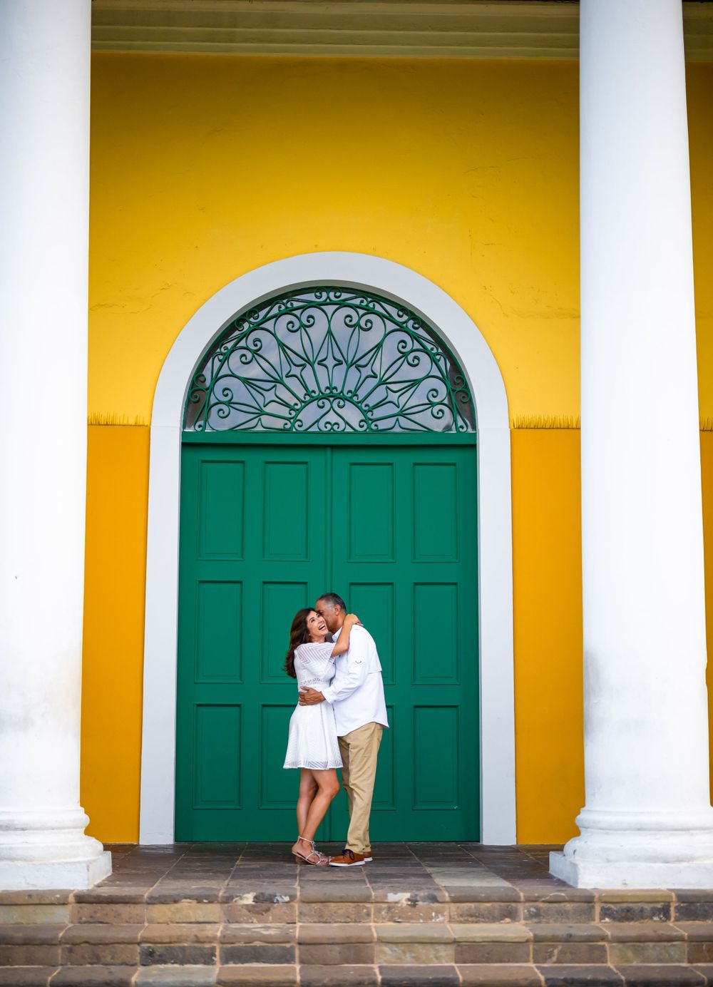 Romantic moment in front of vibrant yellow wall and green colonial door.