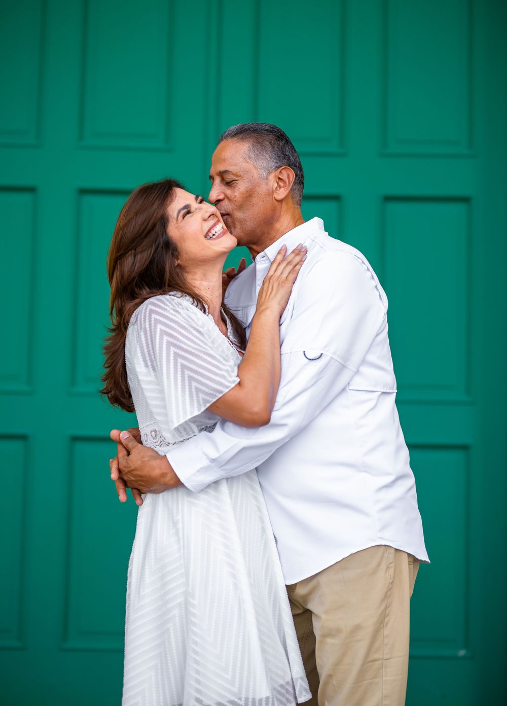 Loving couple in white outfits embracing against vibrant green door background.