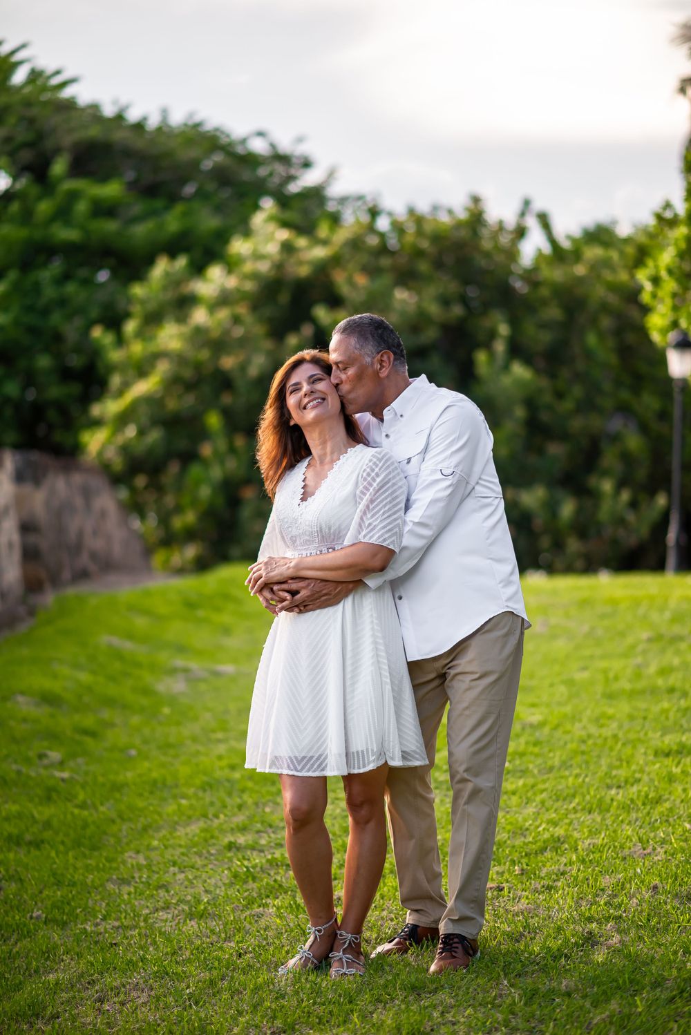 Couple sharing tender moment on grassy hill with garden backdrop.