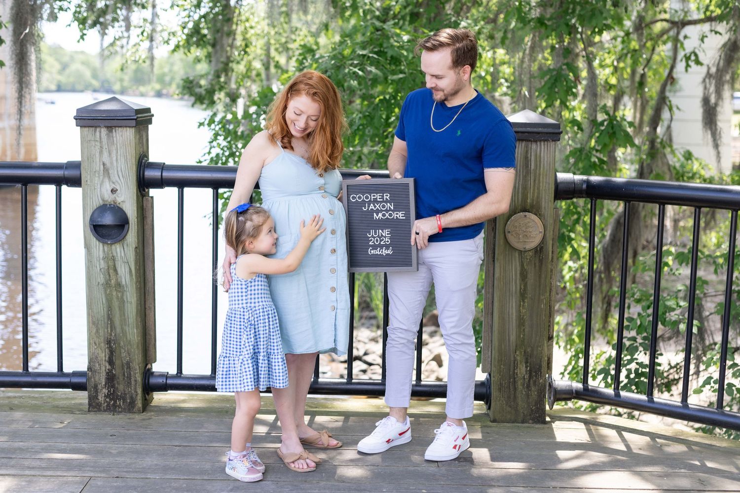 Happy couple while daughter holding ultrasound print in outdoor maternity photo near Lake Erie, captured by Tasha Cannaday.