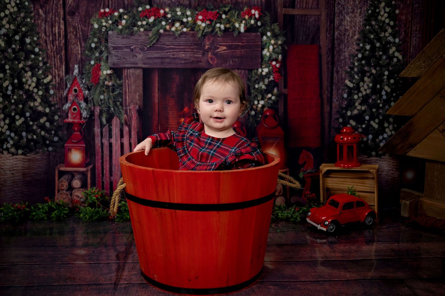 Small child sitting in a red barrel with Christmas decorations in the background.