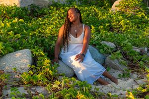 Someone in a white sundress sits among yellow wildflowers and rocks during golden hour lighting.