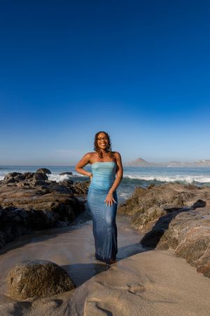 Scenic coastal photo series showing someone in blue dress posing on rocky beach with mountains and ocean in background.