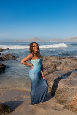A series of photos shows someone in a flowing blue dress posing on rocky coastal terrain with ocean waves and mountains visible.