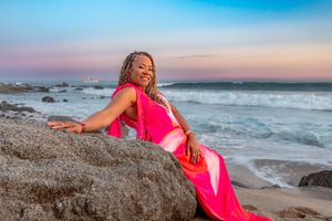 Scenic coastal views at sunset with pink dress accents against rocky beach formations and crashing waves.