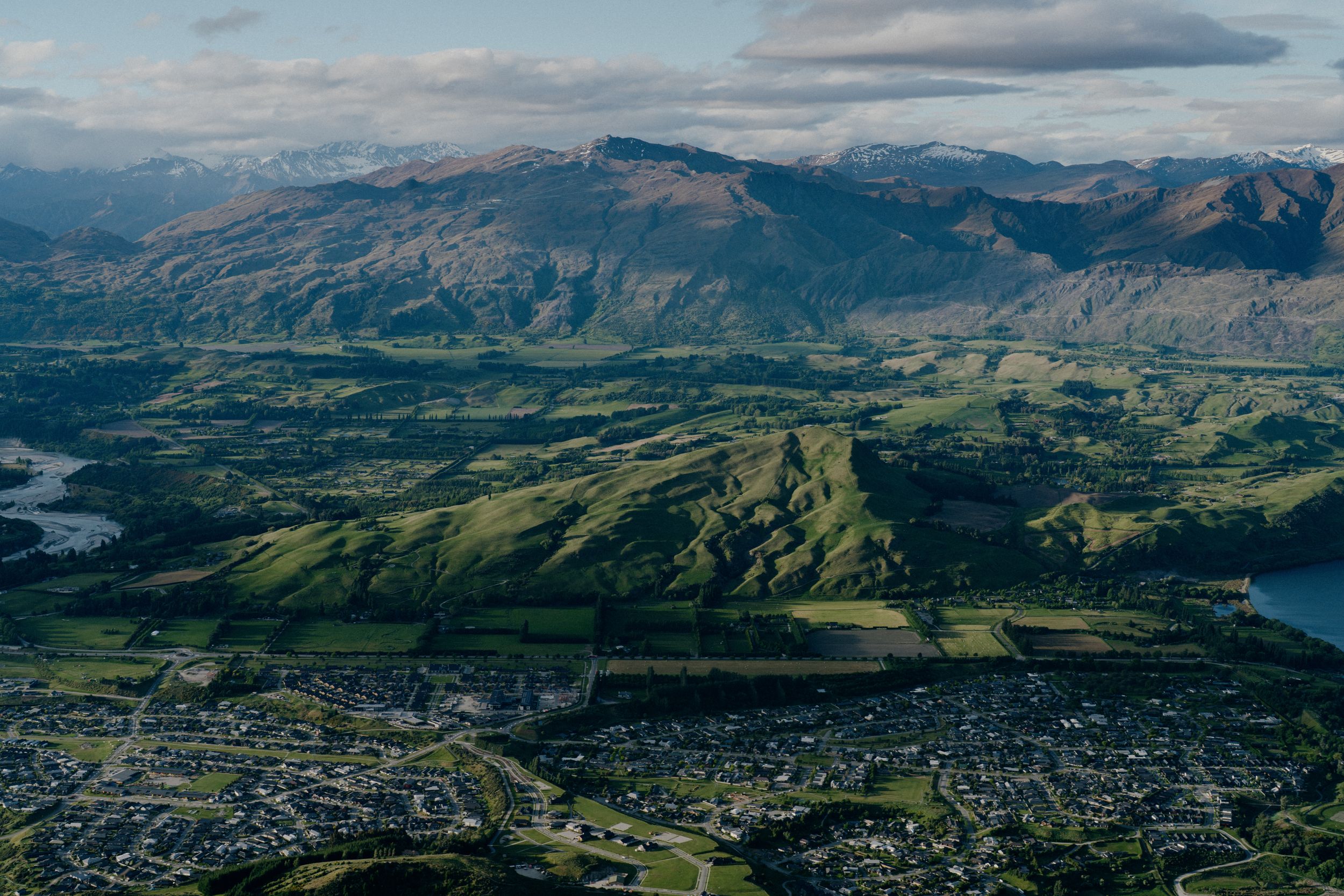 Aerial view of a sprawling town nestled among green mountains with lakes in the distance.