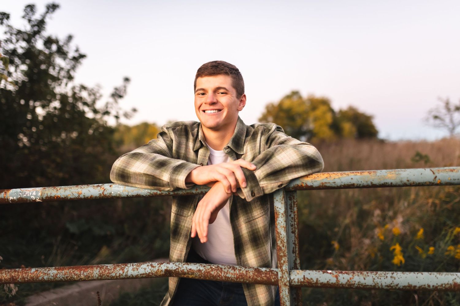 Portrait of a senior boy leaning on a rusty fence during autumn senior photo session.