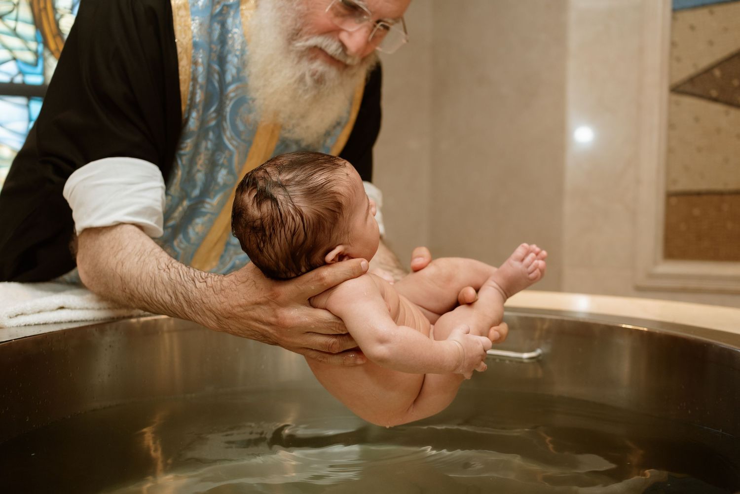 A religious ceremony takes place as a baby is lifted up during what appears to be a baptism or blessing ritual.